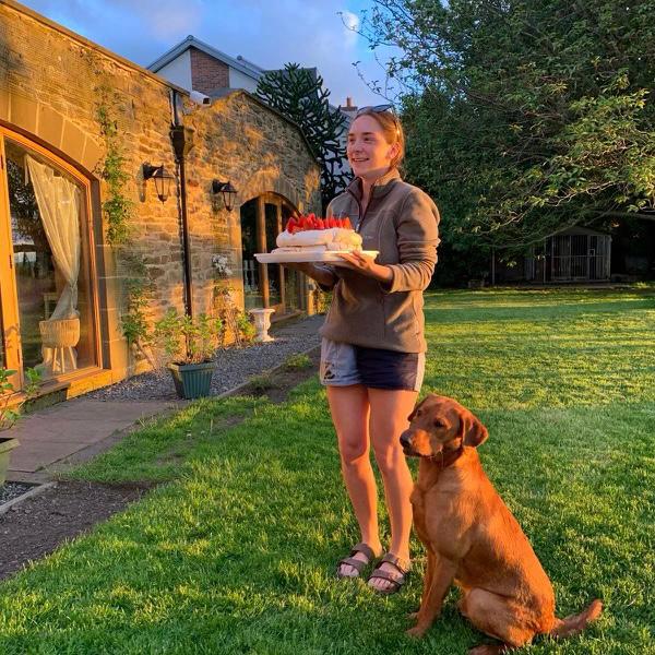 A woman wearing rugby clothing with a cake and a dog