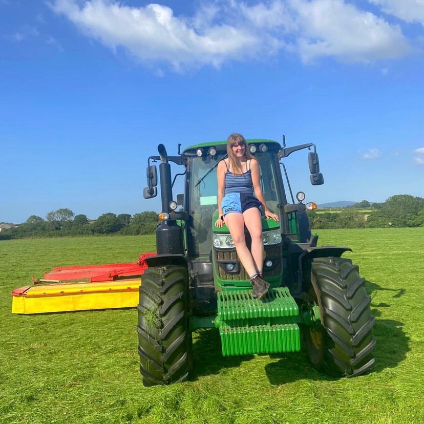 Woman wearing rugby clothing and siting on a farm vehicle