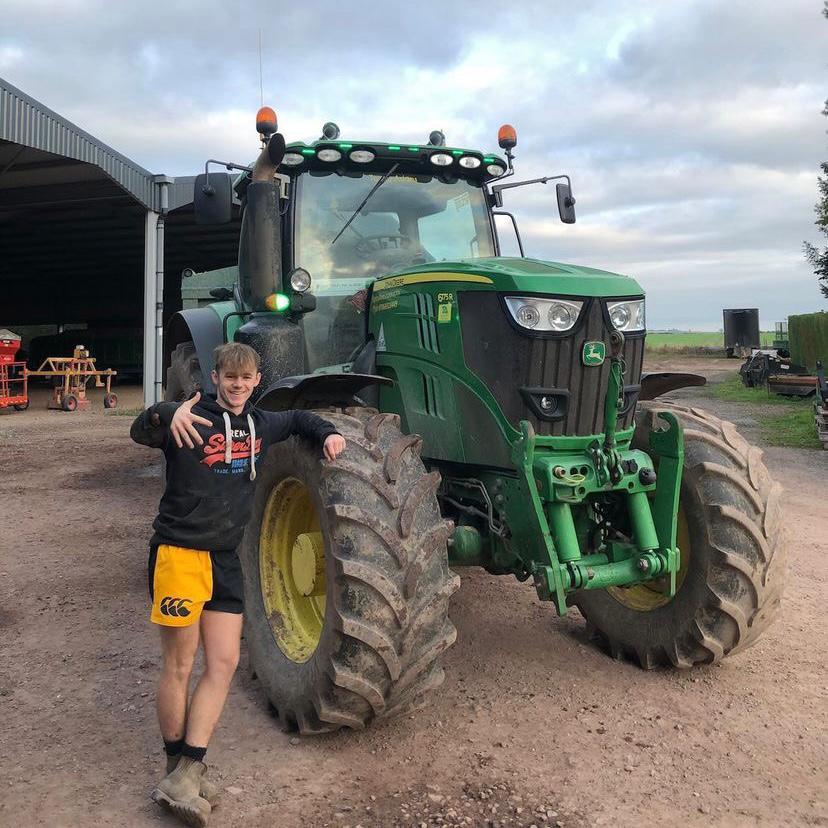 Teen wearing gold and black Canterbury shorts and posing in front of a farm vehicle