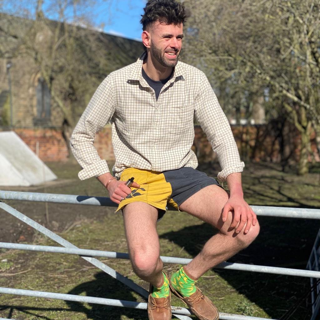 Man wearing gold and black canterbury shorts and sitting on a fence