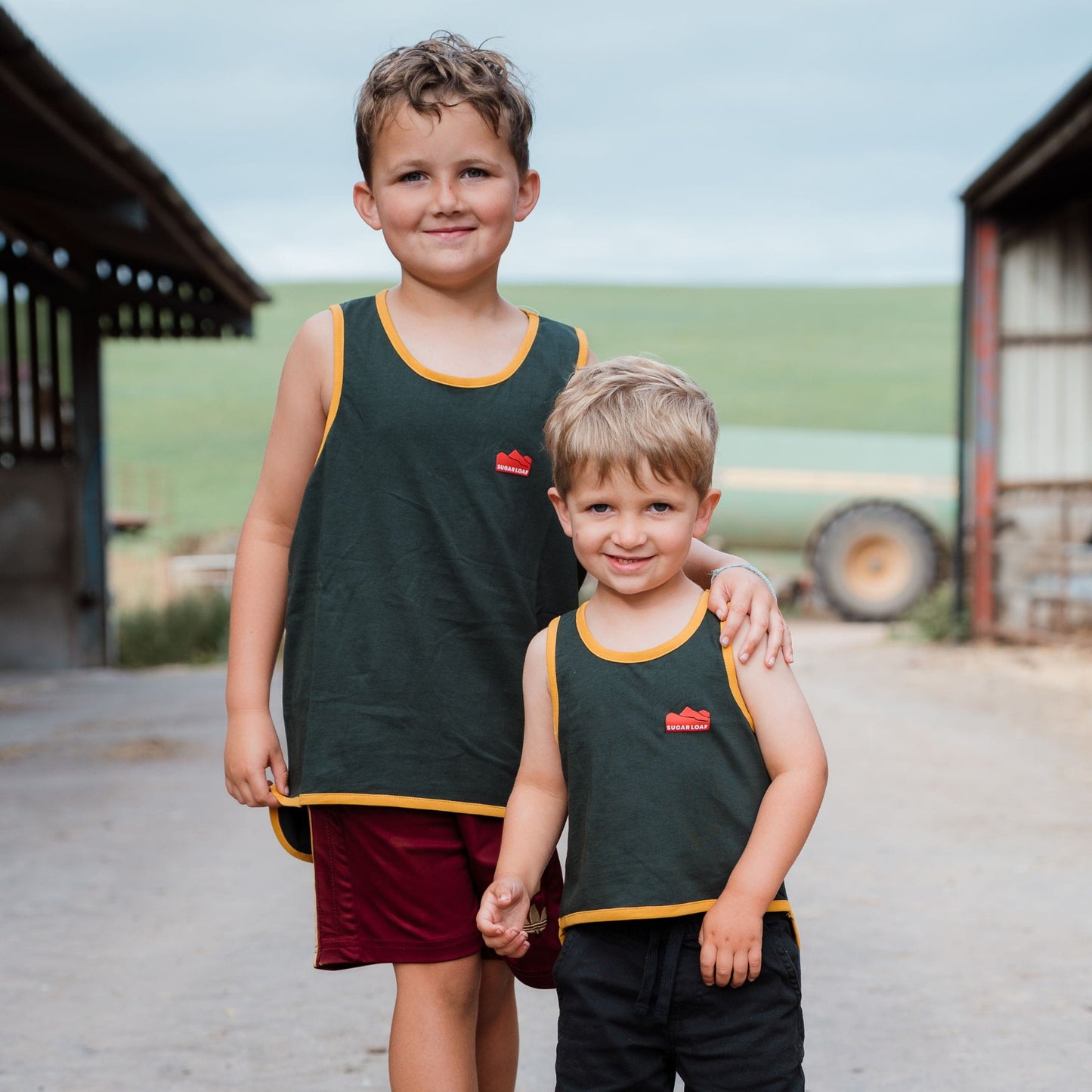 Children wearing Sugar Loaf Kids Rascal Shearing Singlet in Green and Gold on a farm.